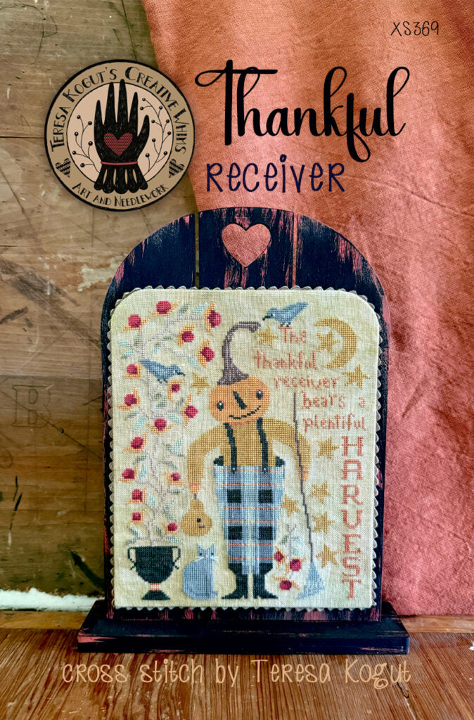 Cross stitch art 'Thankful Receiver' by Teresa Kogut, featuring colorful harvest theme and wooden display.