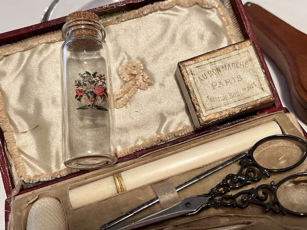 Antique sewing kit with floral glass vial, scissors, and tools, featuring elegant design and vintage materials.