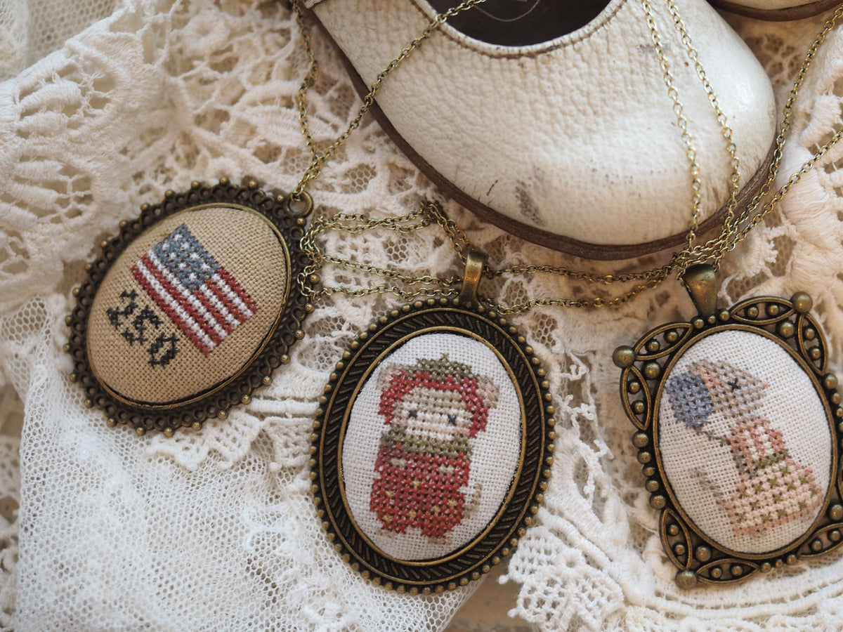 Vintage embroidered pendants featuring American flag, festive doll, and girl in dress on lace background.