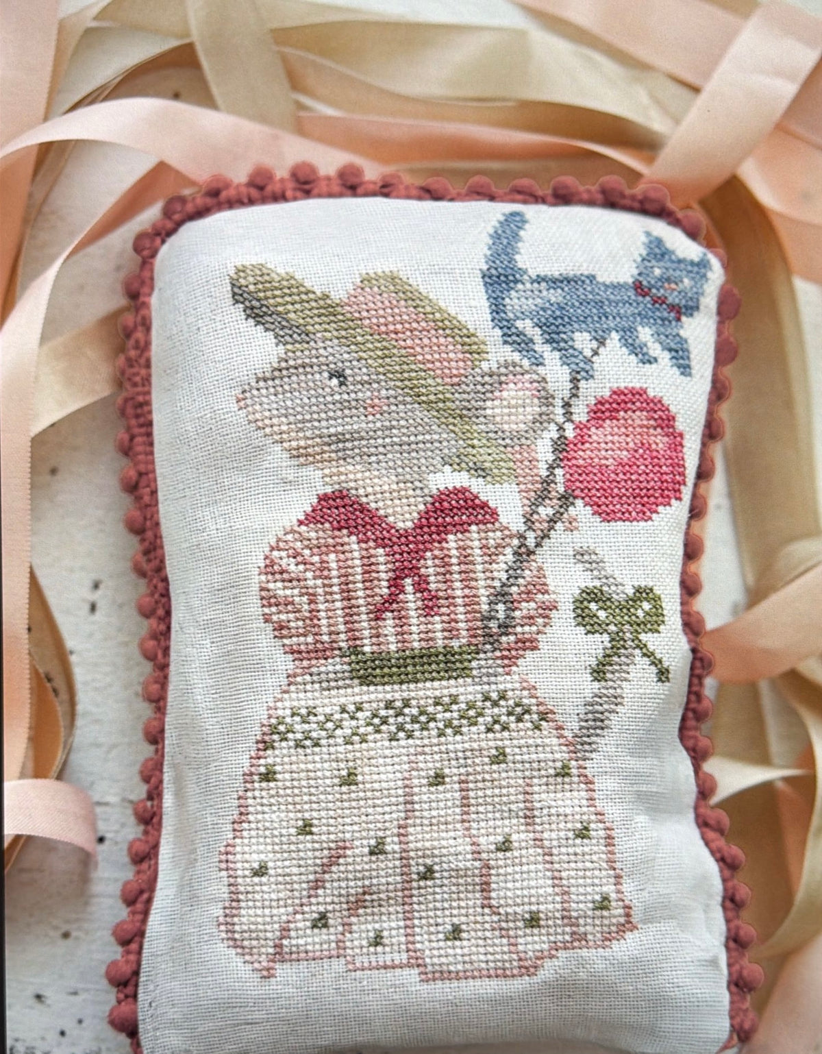 Hand-stitched decorative pillow featuring a mouse in a dress holding balloons, pastel colors, and pom-pom trim.