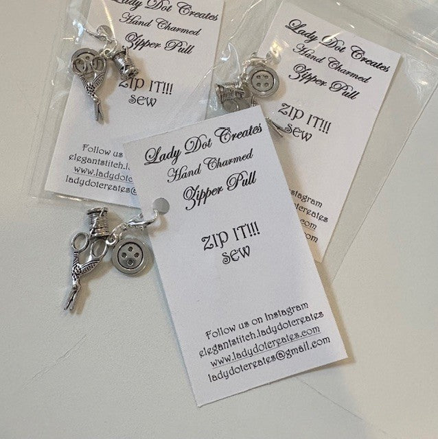 Handcrafted silver zipper pull with sewing scissors and button charms for craft enthusiasts.