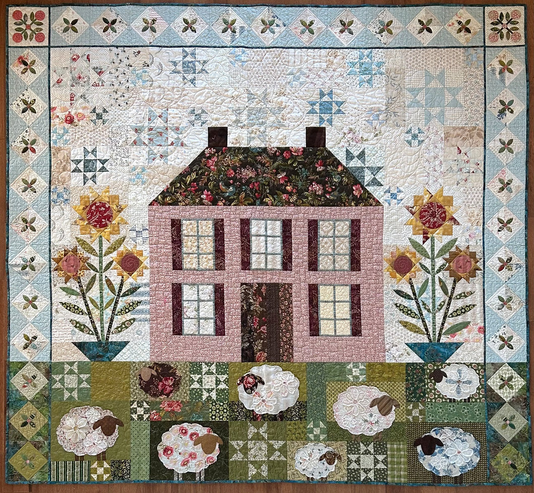 Colorful quilt featuring a house design with flowers and sheep, crafted from assorted fabrics.