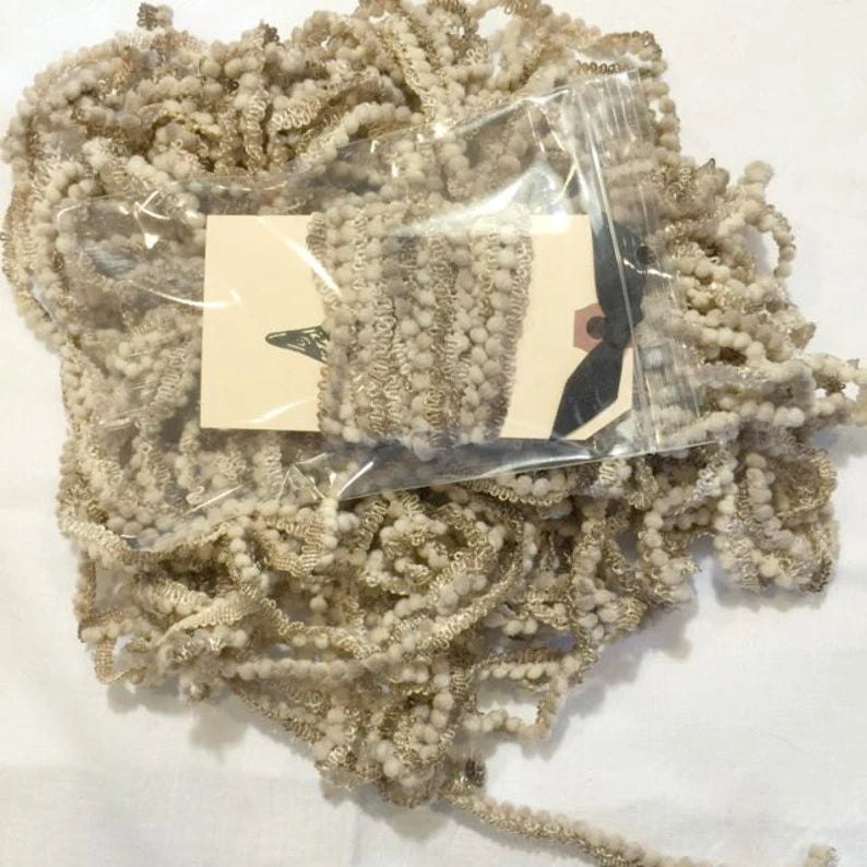 Beige decorative trim ribbon in a pack, featuring textured fabric with pom-pom details for crafting.