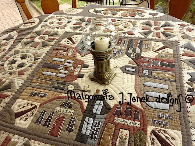 Quilted table cover featuring detailed house designs in warm tones, ideal for home decor.