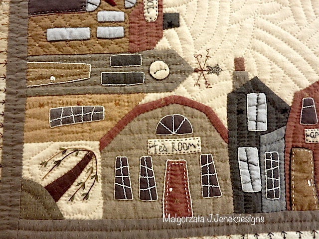 Quilted wall hanging featuring cozy village scenes, earthy tones, and handcrafted details.