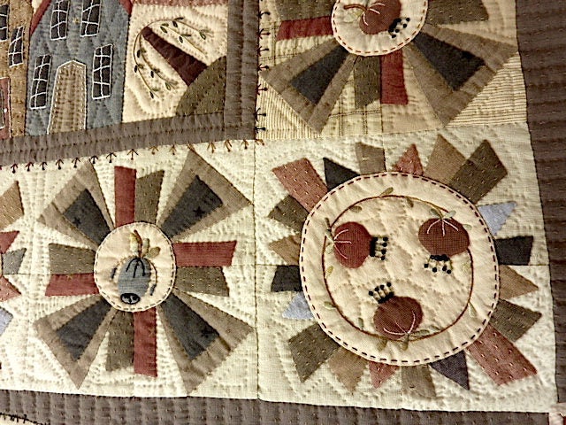 Quilted wall hanging with rustic designs, featuring muted colors and detailed embroidery on cotton fabric.