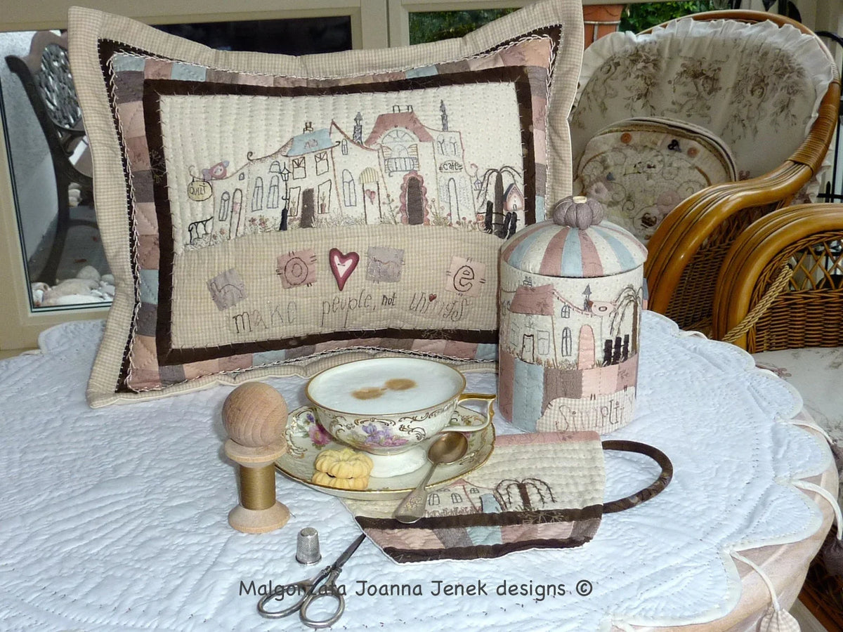 Quilted decorative pillow with whimsical house design in soft pastel colors, ideal for home decor.