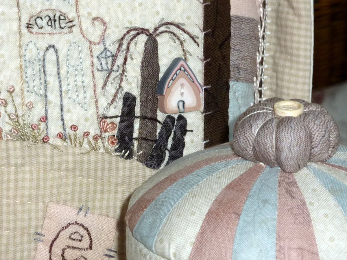 Quilted fabric decoration featuring a cafe, pastel colors, and a pumpkin-shaped pin cushion.