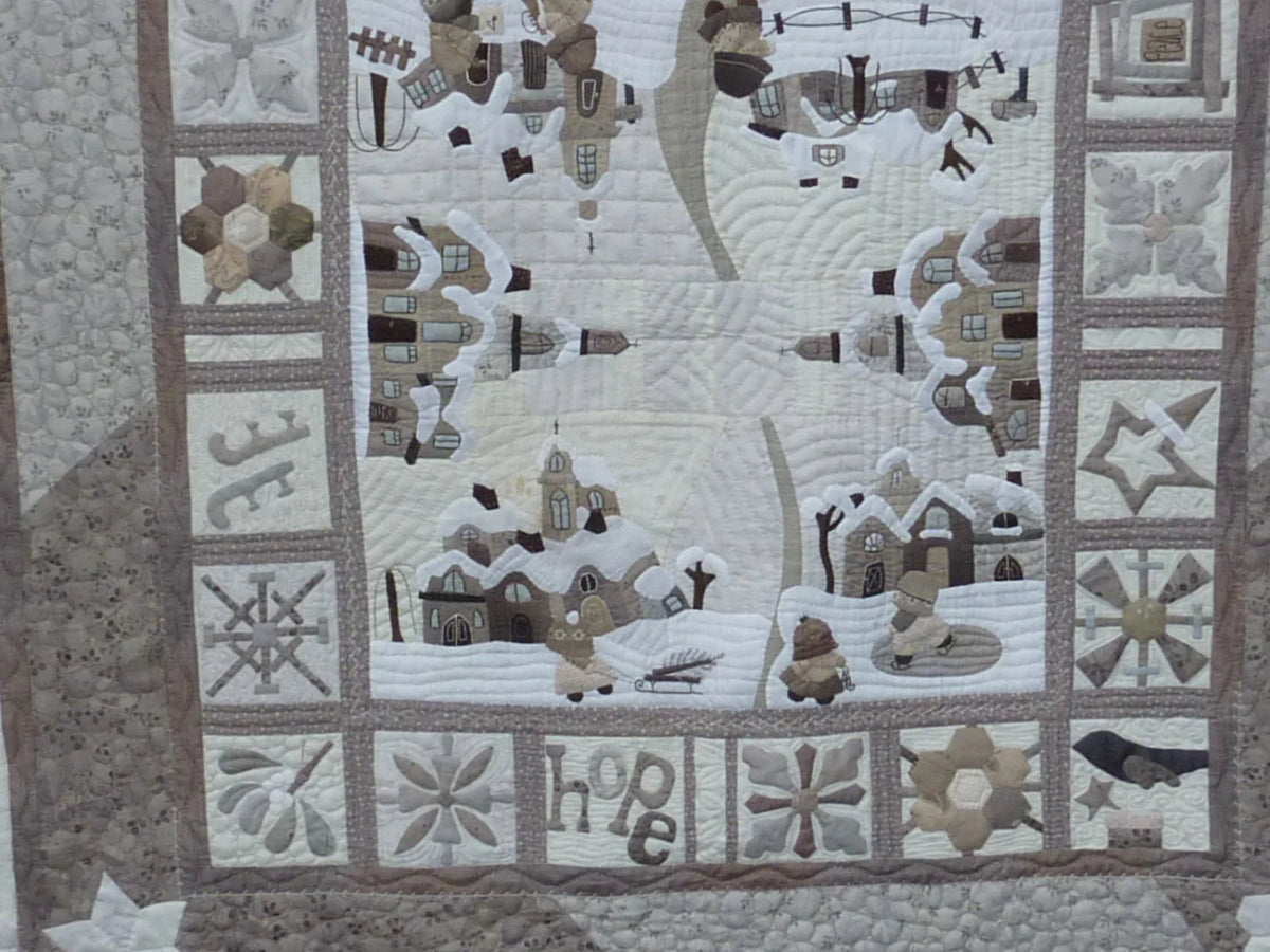 Winter-themed patchwork quilt in neutral tones featuring cozy village scenes and stitched details.
