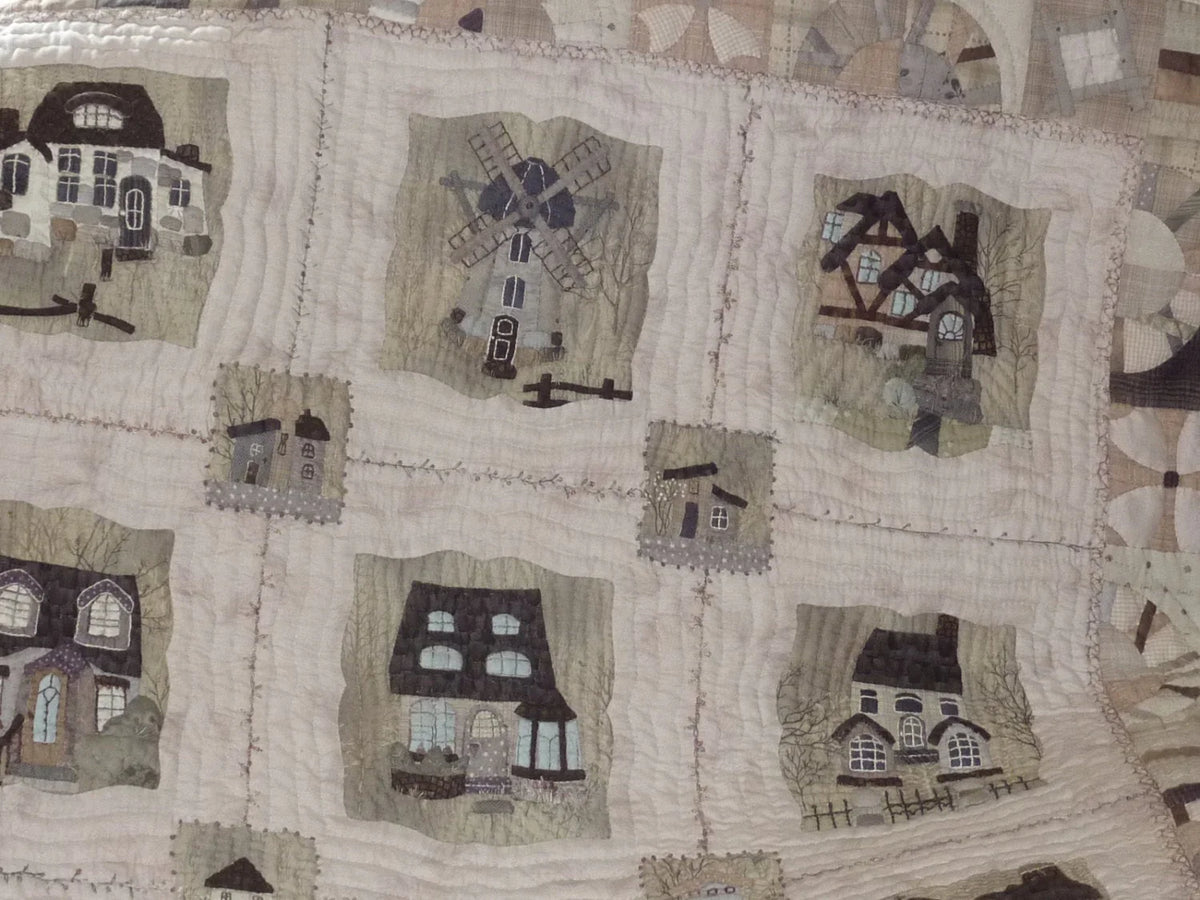 Quilt featuring cozy house and windmill designs in neutral tones, crafted from soft cotton material.