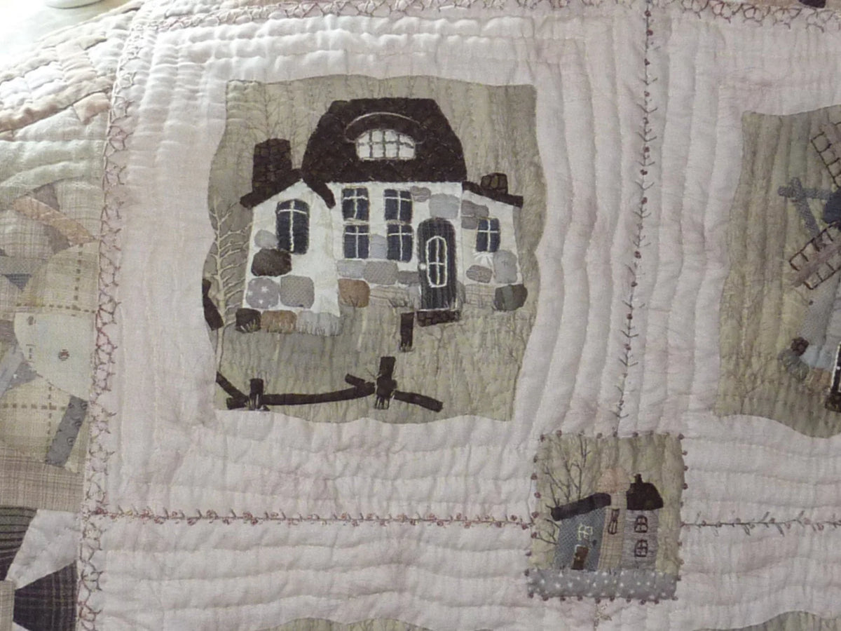 Quilt featuring a charming house design in neutral colors with intricate stitching and textured fabric.
