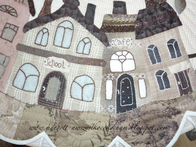 Quilted fabric wall hanging featuring charming houses labeled 'School' and 'Cafe', in muted colors and detailed stitching.
