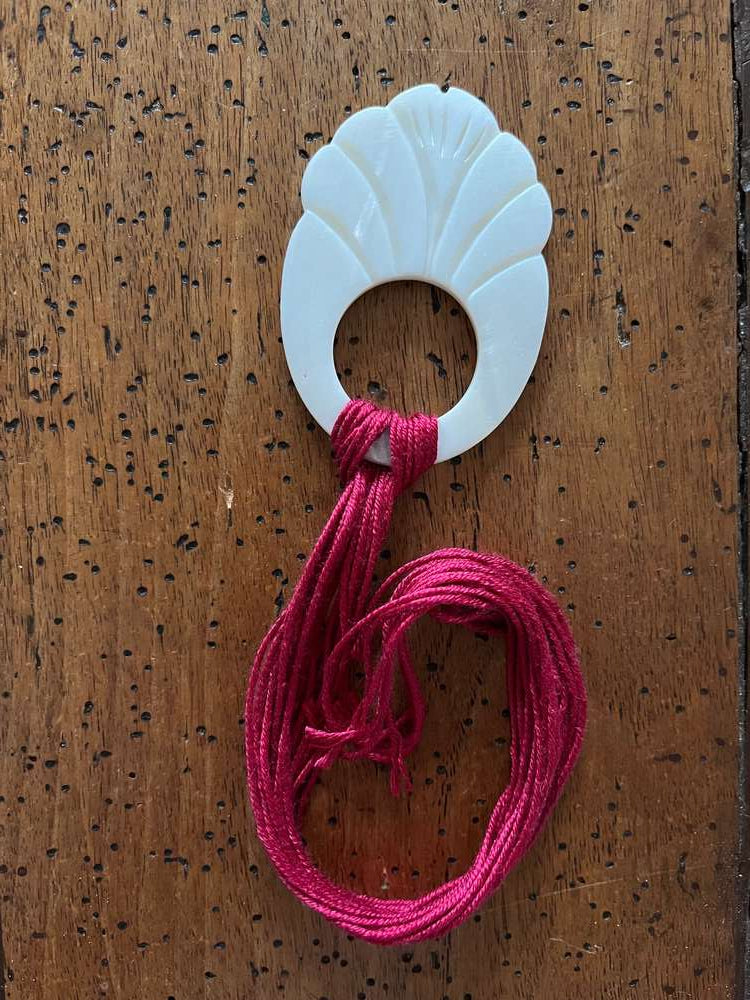 Decorative shell-shaped hair accessory in white with pink cord for stylish updos or braids.