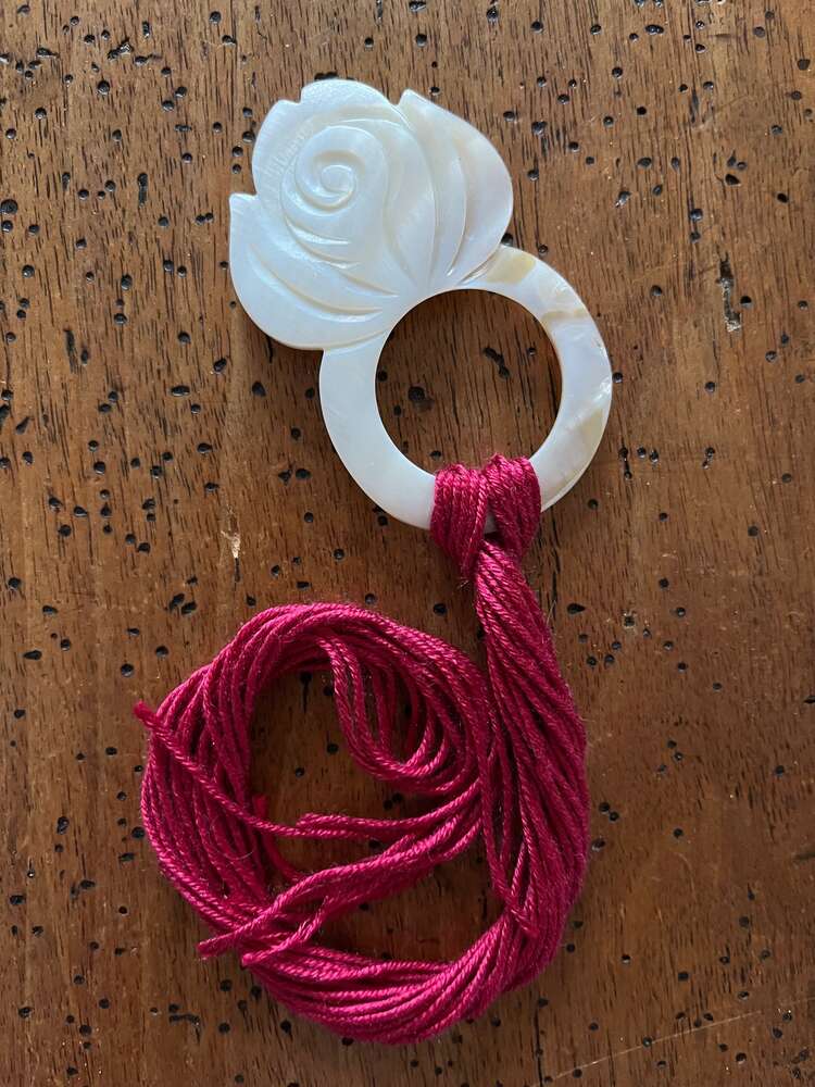White rose-shaped carved ring with red embroidery thread for handmade crafts.