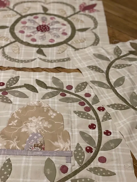 Decorative quilt patchwork featuring floral patterns, beige and green colors, and intricate embroidery details.