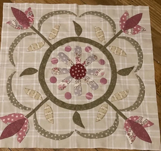 Floral quilt block with pink and beige appliqué on plaid fabric, perfect for crafting and home decor.
