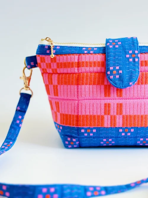 Colorful fabric handbag in blue, pink, and red with zipper closure and adjustable strap.