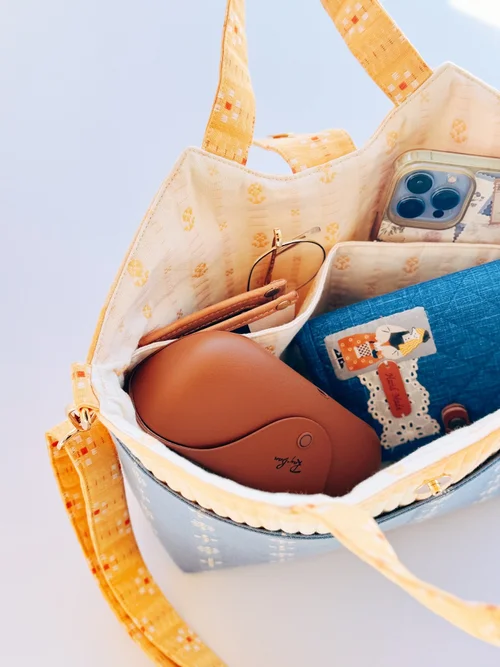 Stylish blue tote bag with yellow handles, featuring a spacious interior for sunglasses, phone, and wallet.