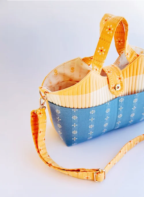 Colorful fabric handbag in blue and yellow with floral pattern, featuring a detachable strap and pleated design.