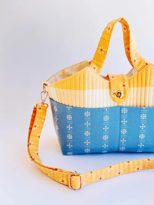 Colorful quilted handbag featuring yellow and blue fabric, with floral patterns and a detachable strap.