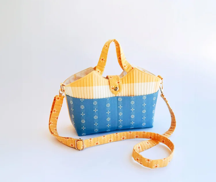 Stylish blue and yellow handbag with quilted design, adjustable strap, and floral pattern accents.