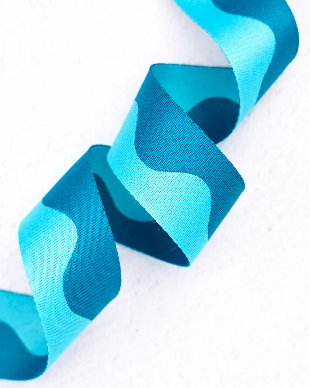 Wavy turquoise satin ribbon, perfect for crafts and gift wrapping, showcasing vibrant blue shades.