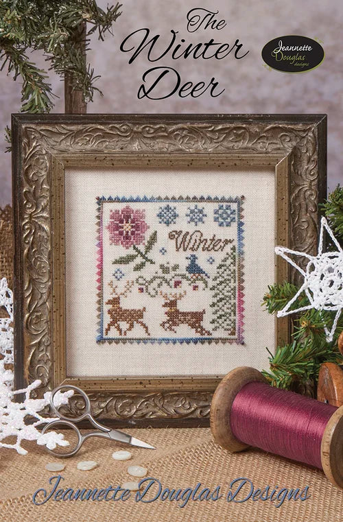 Framed winter-themed cross-stitch design featuring deer, flowers, and snowflakes in soft pastel colors.