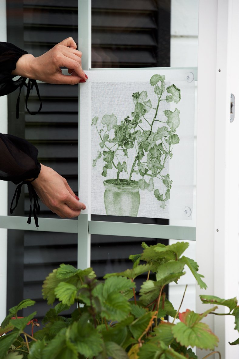 Hand attaching a green botanical print curtain, made from soft fabric, to a window frame.