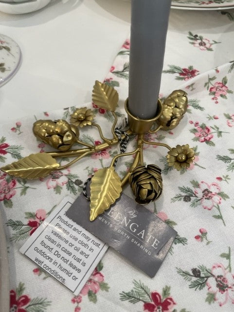 Brass candle holder with floral design, gray candle, and decorative leaves, perfect for home decor.